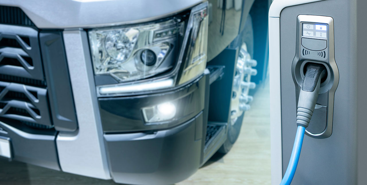 Electric truck charging via heavy-duty EV connector with close-up of front headlight and charging port